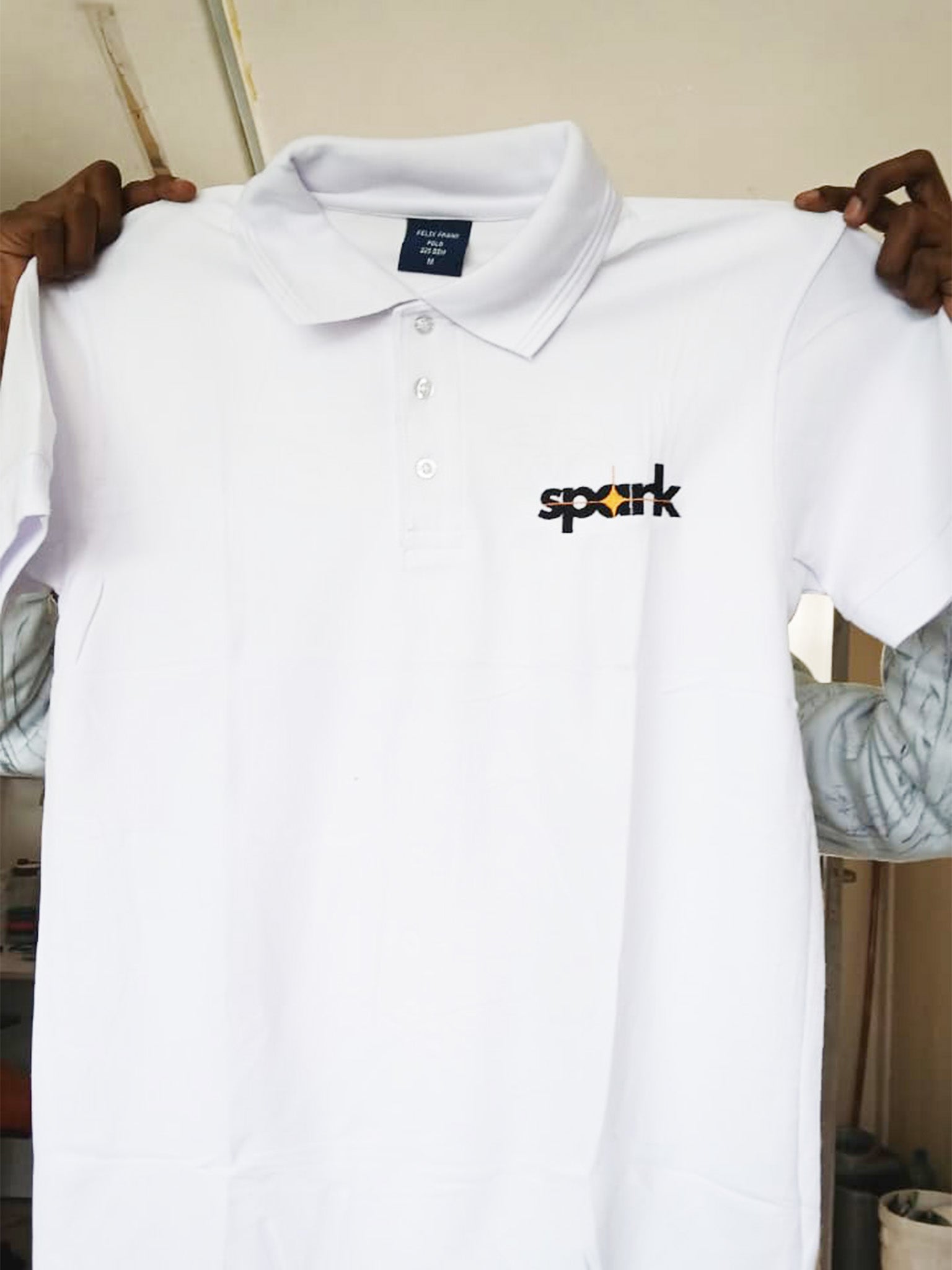 White polo shirt with 'spark' logo on a hanger against a neutral background